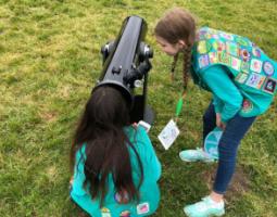 Two girl scouts use a telescope outside.