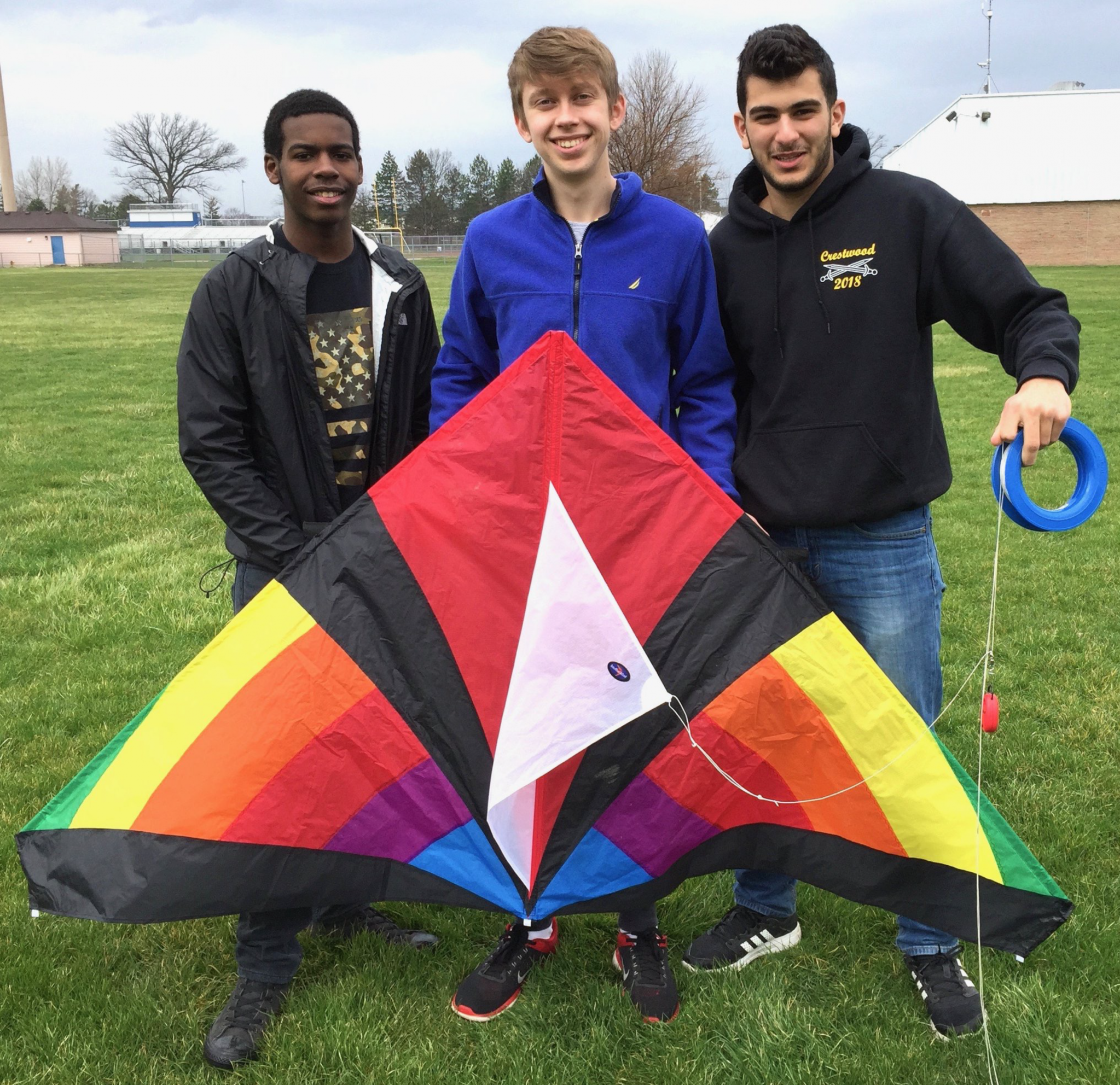 Photo of three boys standing in a field with a colorful kite