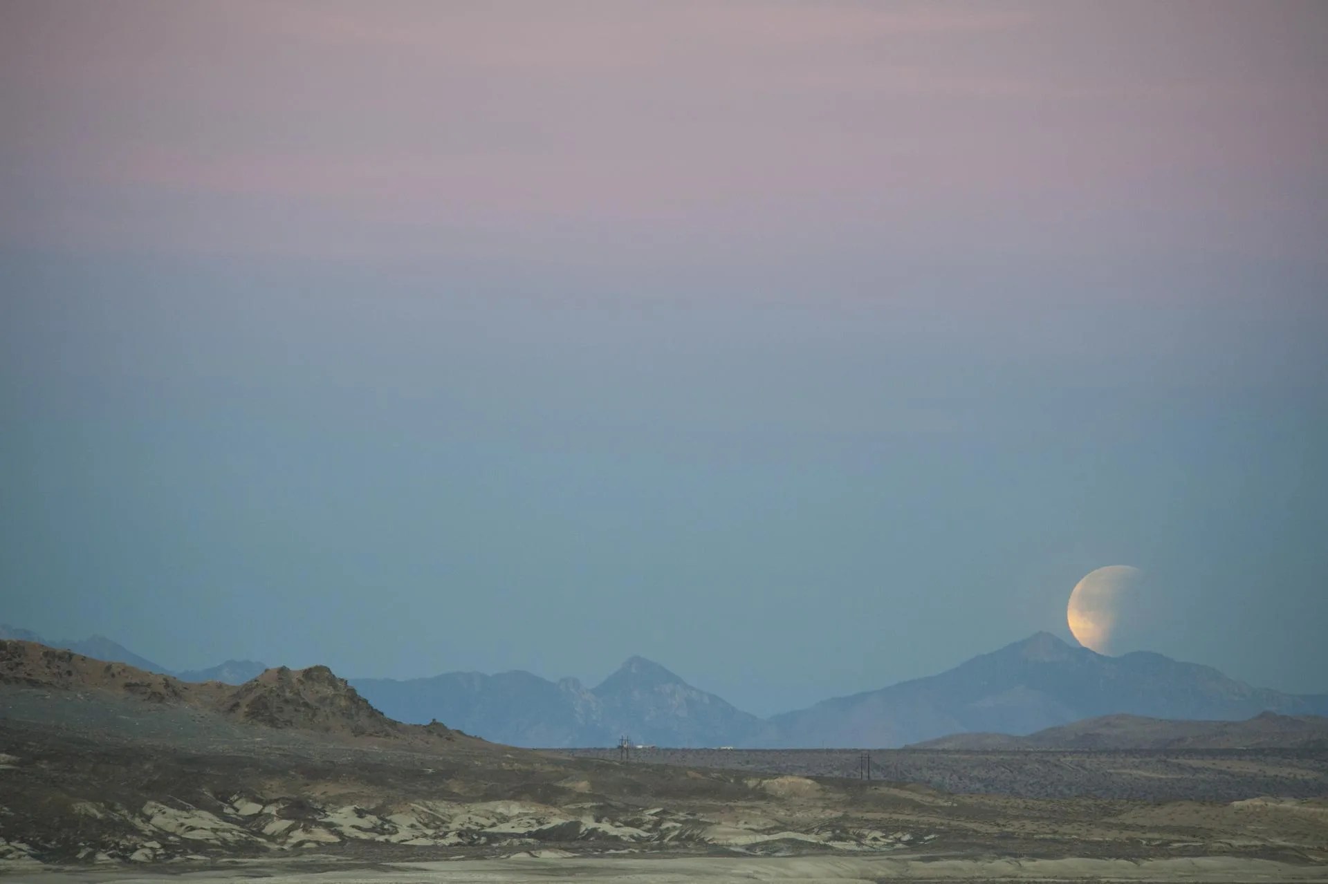 moon setting over desert landscape