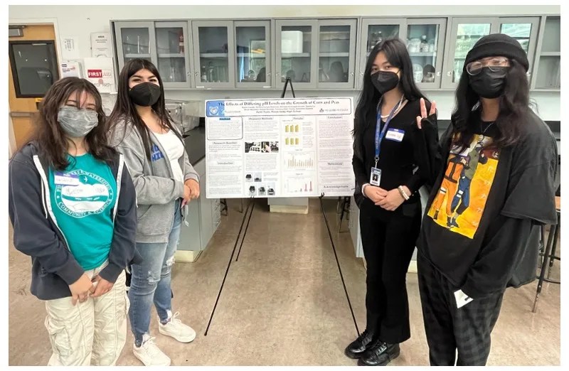Photo of four students from the GLOBE Student Research Symposium for northern California schools standing next to their poster.