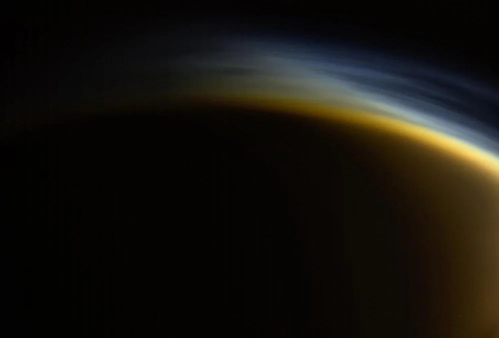 Crescent view of Titan with wispy layers of its atmosphere on top.