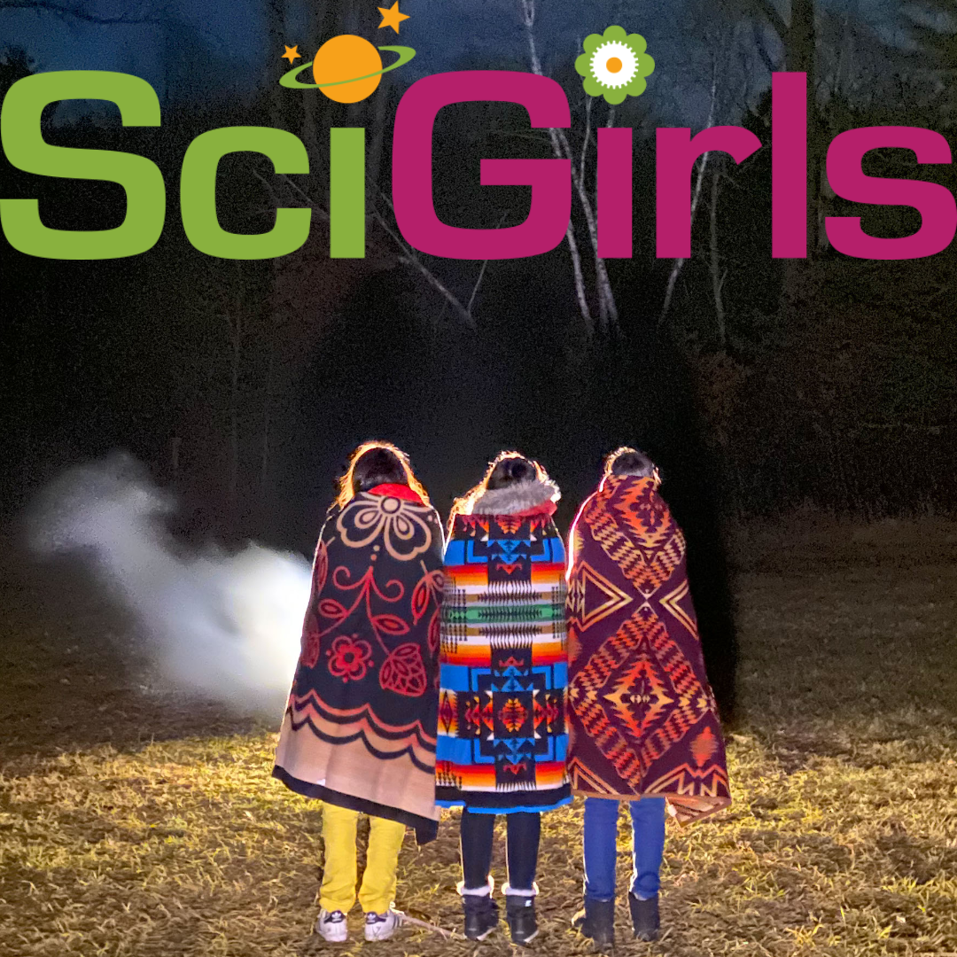 Photo of 3 girls facing away from the camera in a field looking at the night sky, they are each wrapped in very colorful blankets.