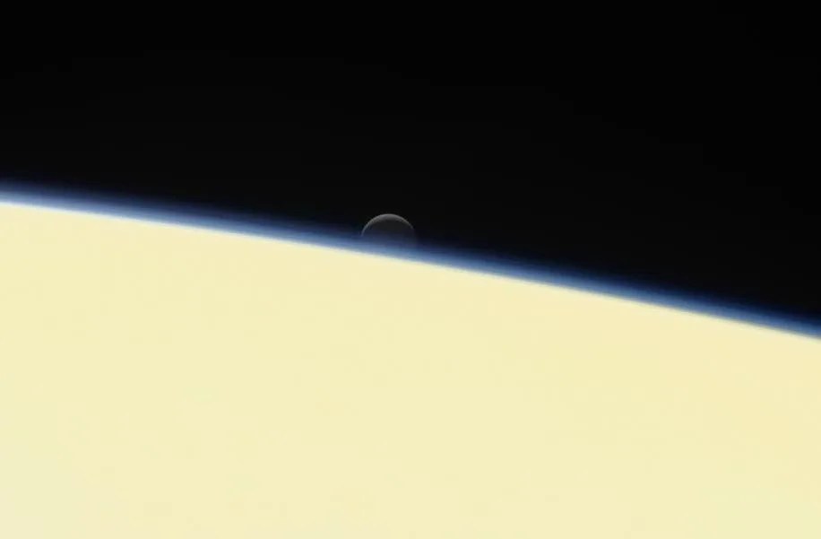 Enceladus setting behind hazy horizon