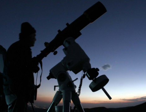 A person standing by a telescope at night, ready to observe transiting exoplanets.