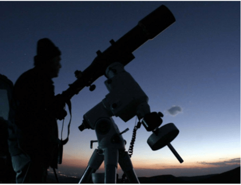 A person standing by a telescope at night, ready to observe transiting exoplanets.
