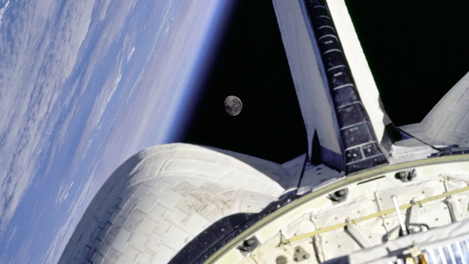 Earth and the Moon as seen over the tail and engines of the Space Shuttle Discovery in orbit.