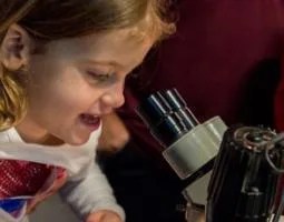 A little girl looks through a telescope