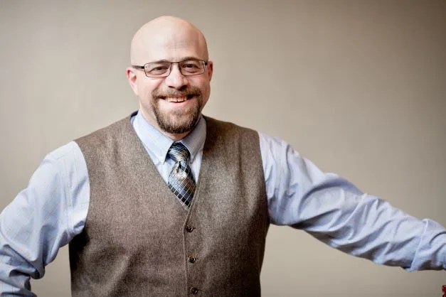 Portrait of Joshua Pepper in a vest, blue tie, and light blue dress shirt.