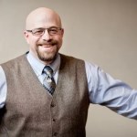 Portrait of Joshua Pepper in a vest, blue tie, and light blue dress shirt.