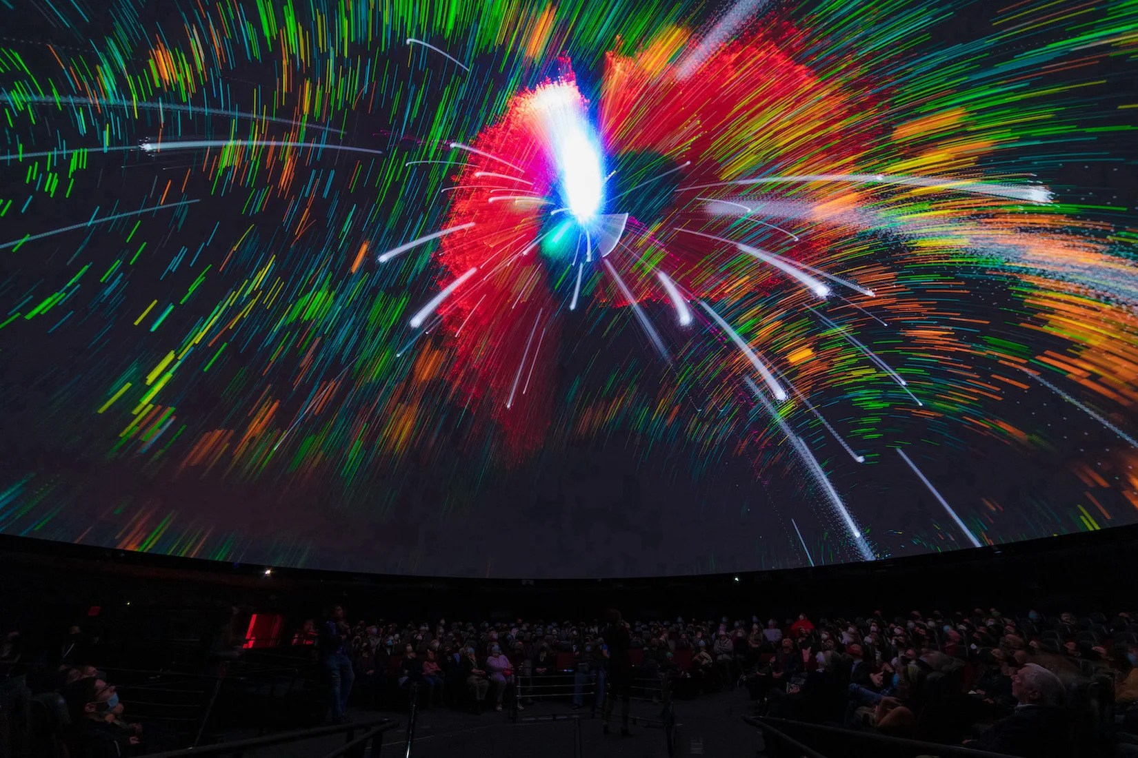 Colored spirals of green, blue and yellow cover the planetarium dome above the audience.