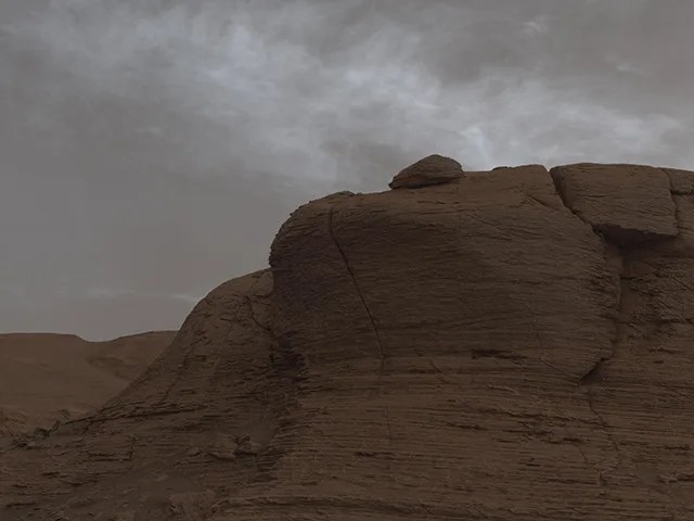 A sandstone peak is shown beneath a cloudy grey sky.