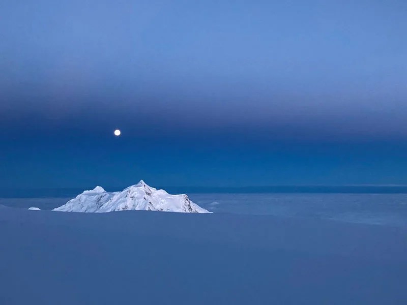 A full moon rises above a snow-capped peak in Alaska.