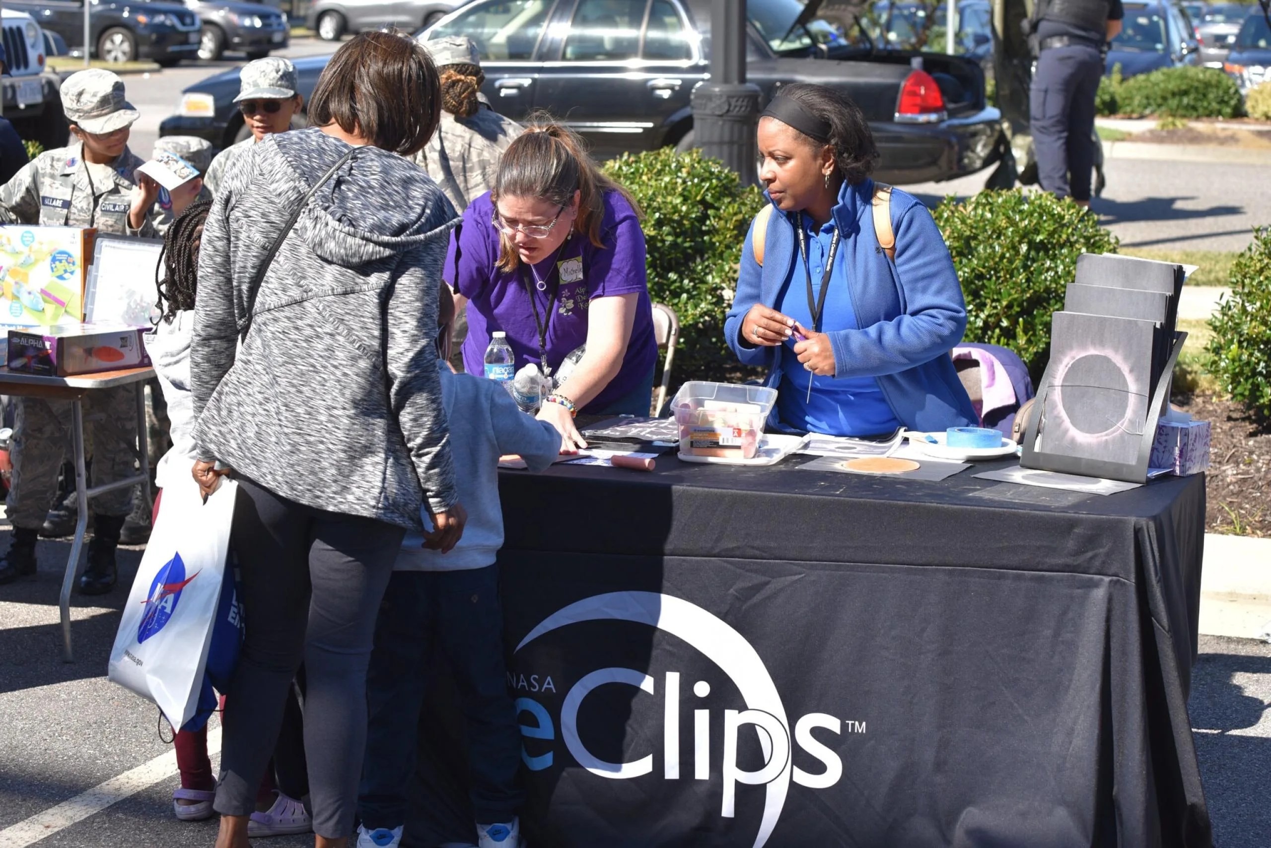 Joan Harper-Neely and volunteer help two young students and an adult to create corona images at the NASA eClips exhibit table.