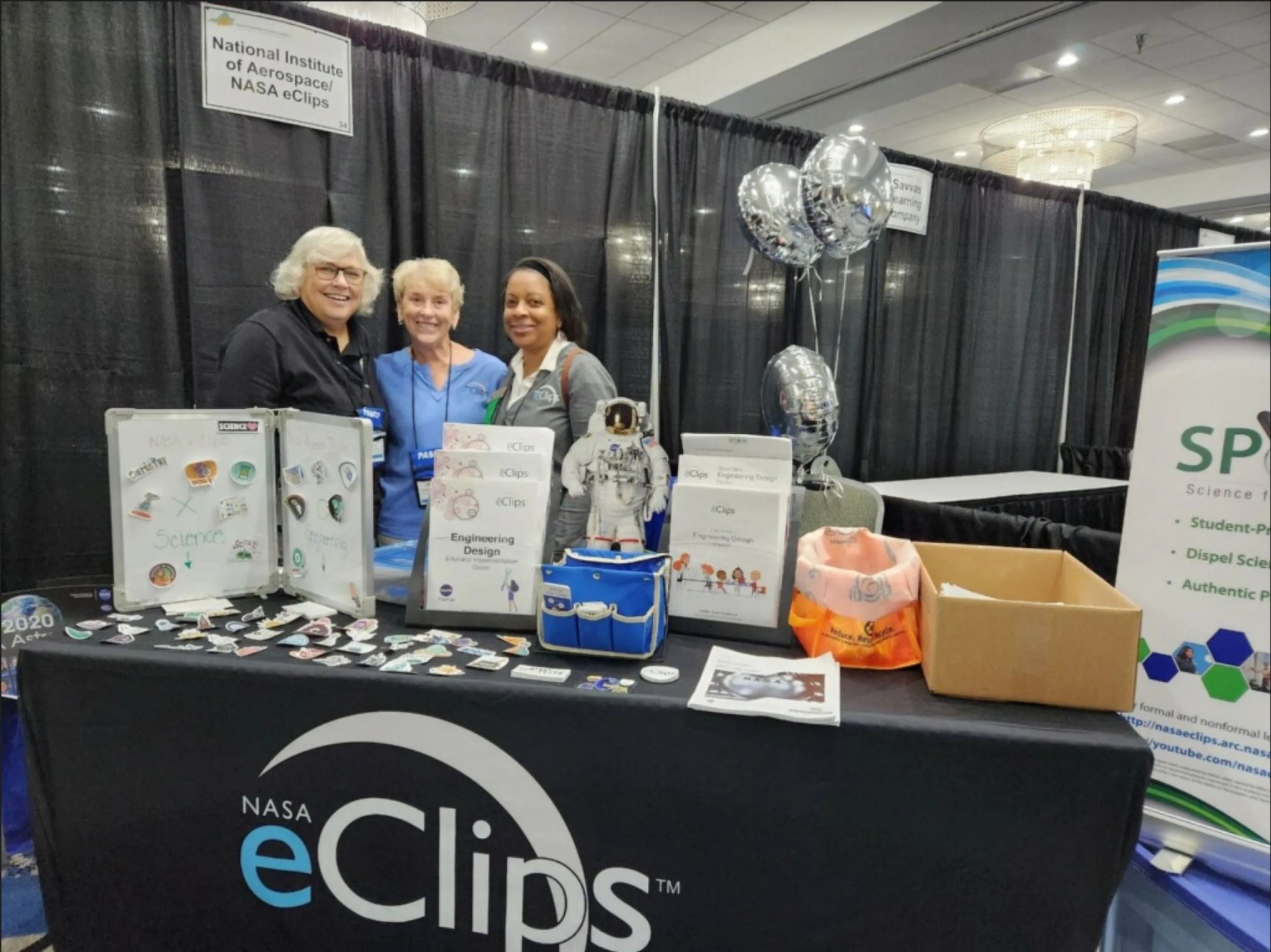 Betsy McAllister, Sharon Bowers, and Joan Harper-Neely stand at the NASA eClips exhibit booth displaying educational materials during the VAST Professional Develoment Institute.