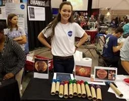 A female high school student in a NASA t-shirt stands behind a table with a sun exhibit