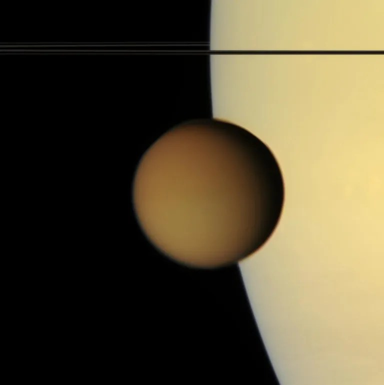 The murky orange disk of Saturn's moon Titan glides past -- a silent, floating sphere transiting Saturn. Titan's photochemical smog completely obscures the surface in such natural color views. Its high-altitude hazes are visible against the disk of Saturn as they attenuate the light reflected by the planet.
