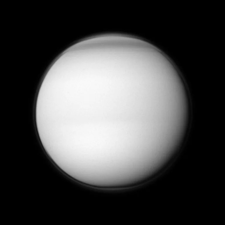 The Cassini spacecraft examines Titan's north polar hood, the part of the atmosphere of Saturn's largest moon appearing dark at the top of this image. The image was taken in visible violet light with the Cassini spacecraft wide-angle camera on April 19, 2011.
