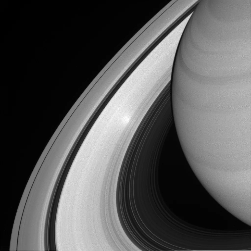 Black and white of Saturn and rings with an extra bright spot on them.