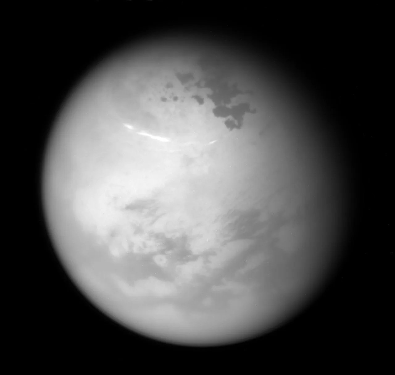 NASA's Cassini spacecraft sees bright methane clouds drifting in the summer skies of Saturn's moon Titan, along with dark hydrocarbon lakes and seas clustered around the north pole. › Full image and caption