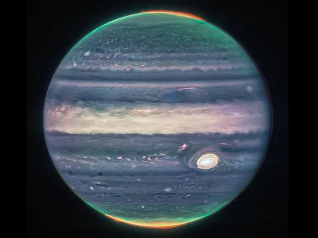Auroras and hazes glow in this composite image of Jupiter. Since infrared light is invisible to the human eye, the light has been mapped onto the visible spectrum: the auroras are mapped to redder colors, hazes to yellows and greens, and light reflected from a deeper main cloud to blues. Jupiter's Great Red Spot is seen as a prominent yellow-white oval at the bottom right.
