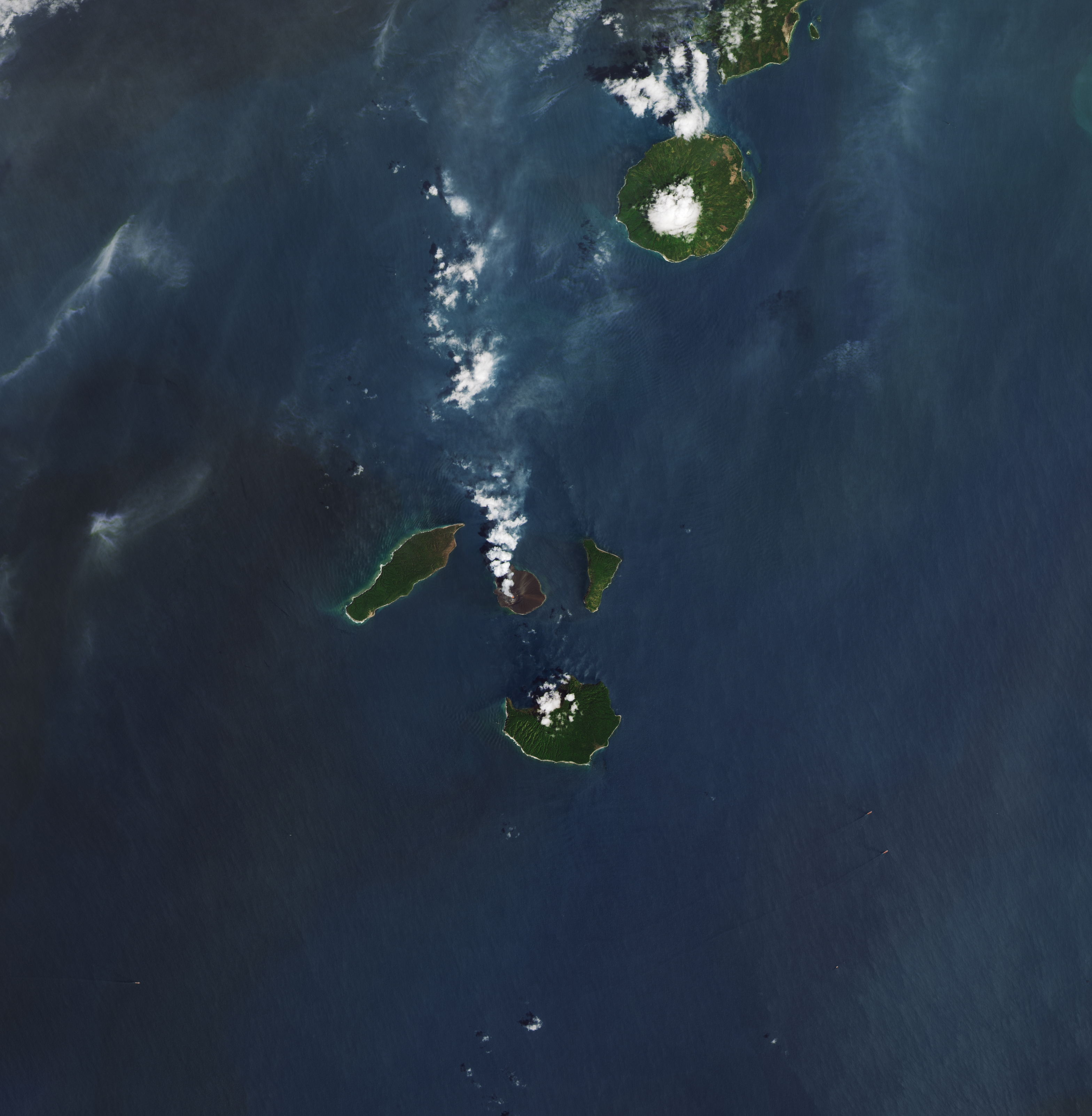 Arial shot of three islands, the center - anak krakatau, billowing smoke emits from a red spot