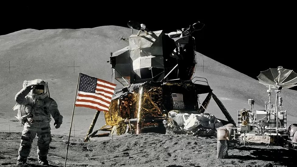 Astronaut on Moon next to American flag, the LEM and moon rover.
