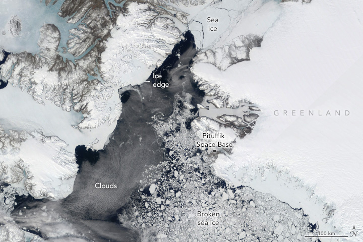 Ice covers the landmass of Greenland (right) and islands of northern Canada (left) with dark waters between and broken sea ice littering the waters.