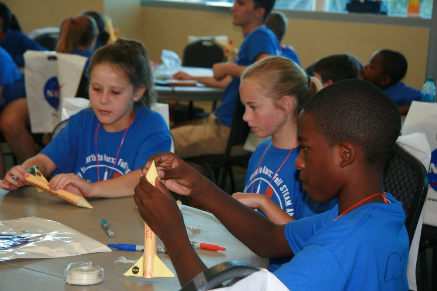 Kids in blue tshirts sitting at a table working on a science project