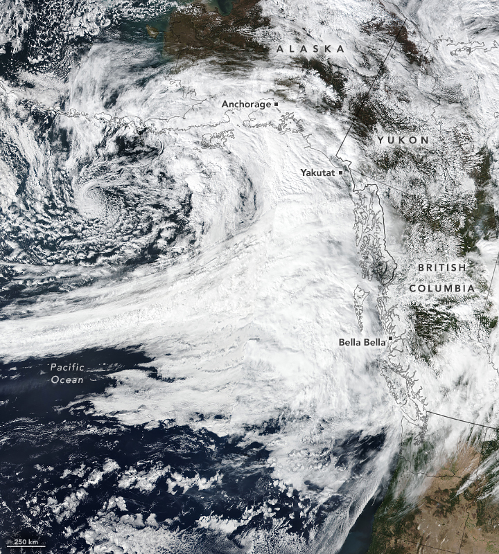 The Northern West Coast of the United States, up to Alaska are pictured. The cities of Bella Bella, Yakutat and Anchorage are labeled and a line of dense cloud cover extends across out into the Pacific Ocean and covers the coastline in clouds.