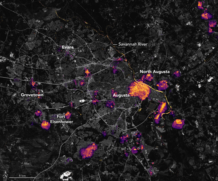 The night satellite image of the greater Augusta area shows gray dark city streets across most of the image with small pockets of orange to purple coloration that indicate lighting.