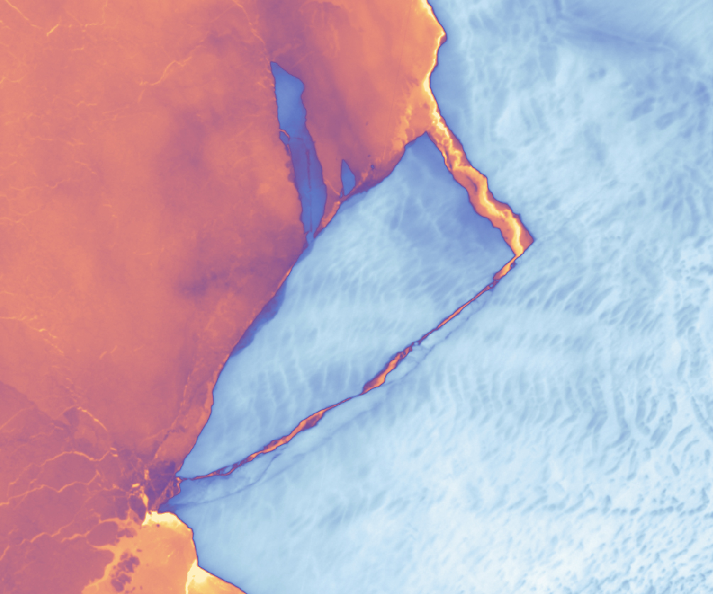 Mostly orange colored ocean water is seen left with light to dark blue ice depicted right. The boundary between them is primarily a diagonal from top center right to lower left. The water nearest the ice takes on a more yellow color than the darker sea to the left, and it cuts down into the ice shelf at a steep angle just below the image top center. The gap between the ice bodies then takes a more narrow 90 degree turn and reconnects to open ocean near the bottom left, creating full separation and an iceberg that is just beginning to depart the ice shelf.