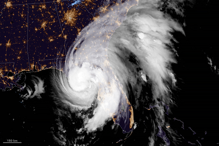 The white large spiral cloud formation of a hurricane can be seen over night imagery of the Southeast United states. The densest part of the storm is over the northern Florida Gulf Coast region, but bands of clouds extend into most of Florida and as far north as North Carolina. City lighting is visible, particularly bright is the Eastern Coast of Florida, and the sprawling lights of greater Atlanta. State borders are superimposed on the land as well.