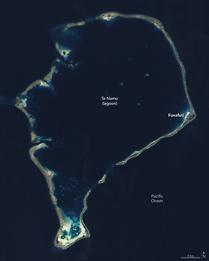 A broken ring of land interrupts the dark blue Pacific Ocean with a lagoon in the interior of the ring.