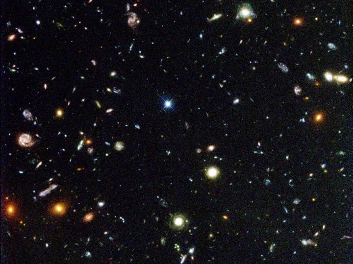 The image is filled with galaxies of various shapes and sizes. Their colors include red, orange, yellow, white, and blue.