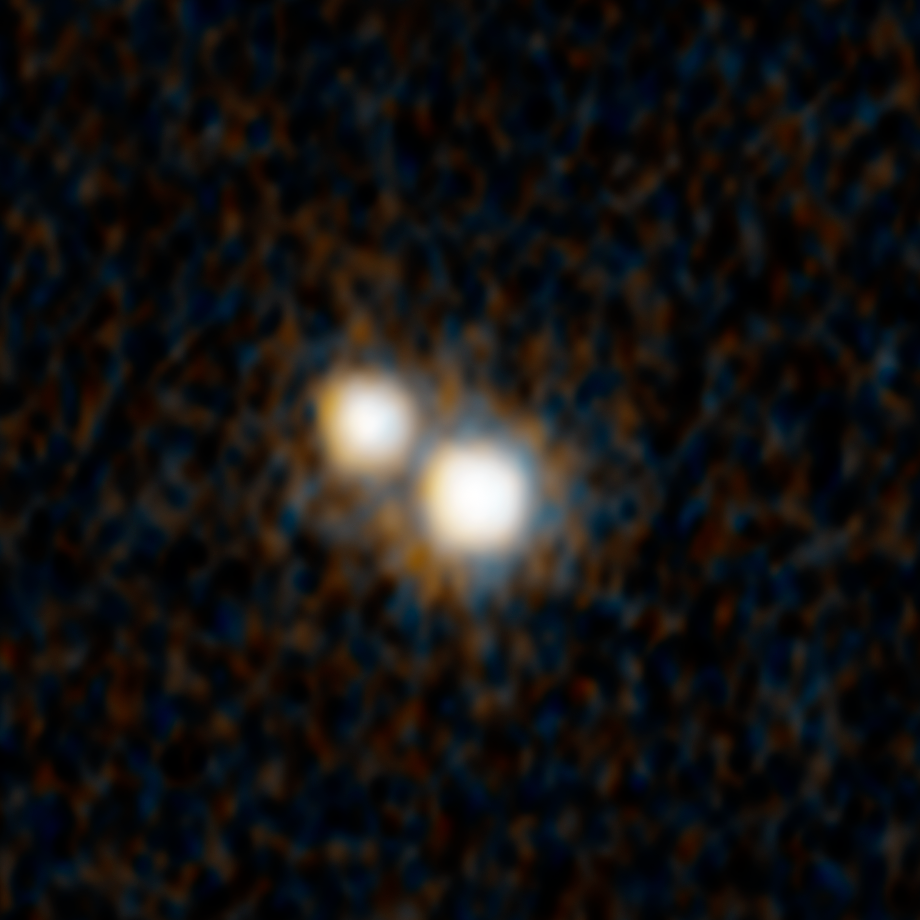 A Hubble photograph of two, closely spaced, white objects, one above and to the left of the other. Each is surrounded by a diffuse orange ring with small orange rays. Black background with very faint brownish orange splotches.