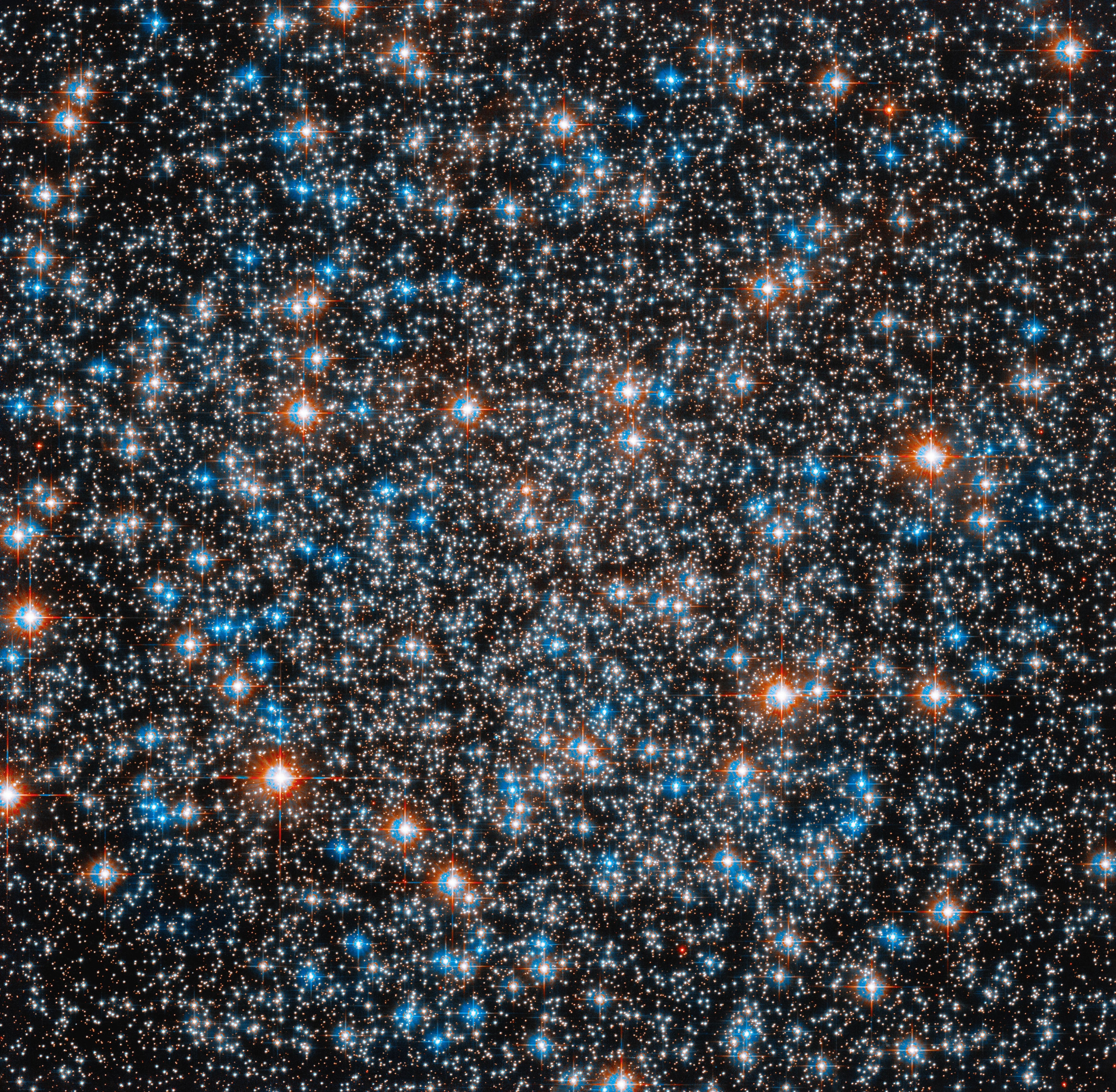 Field is filled with white stars, smattered with blue-white and reddish-orange stars. Stars are concentrated at the center of the image. All are on a black background.