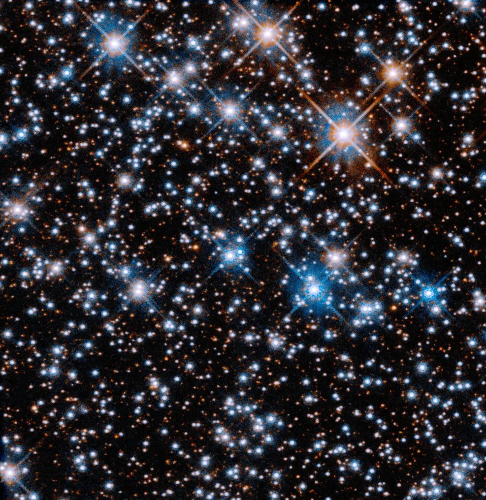 A black background is filled with small, reddish-orange stars. Larger blue-white stars are scattered across the image, with a slightly higher concentration at upper left.