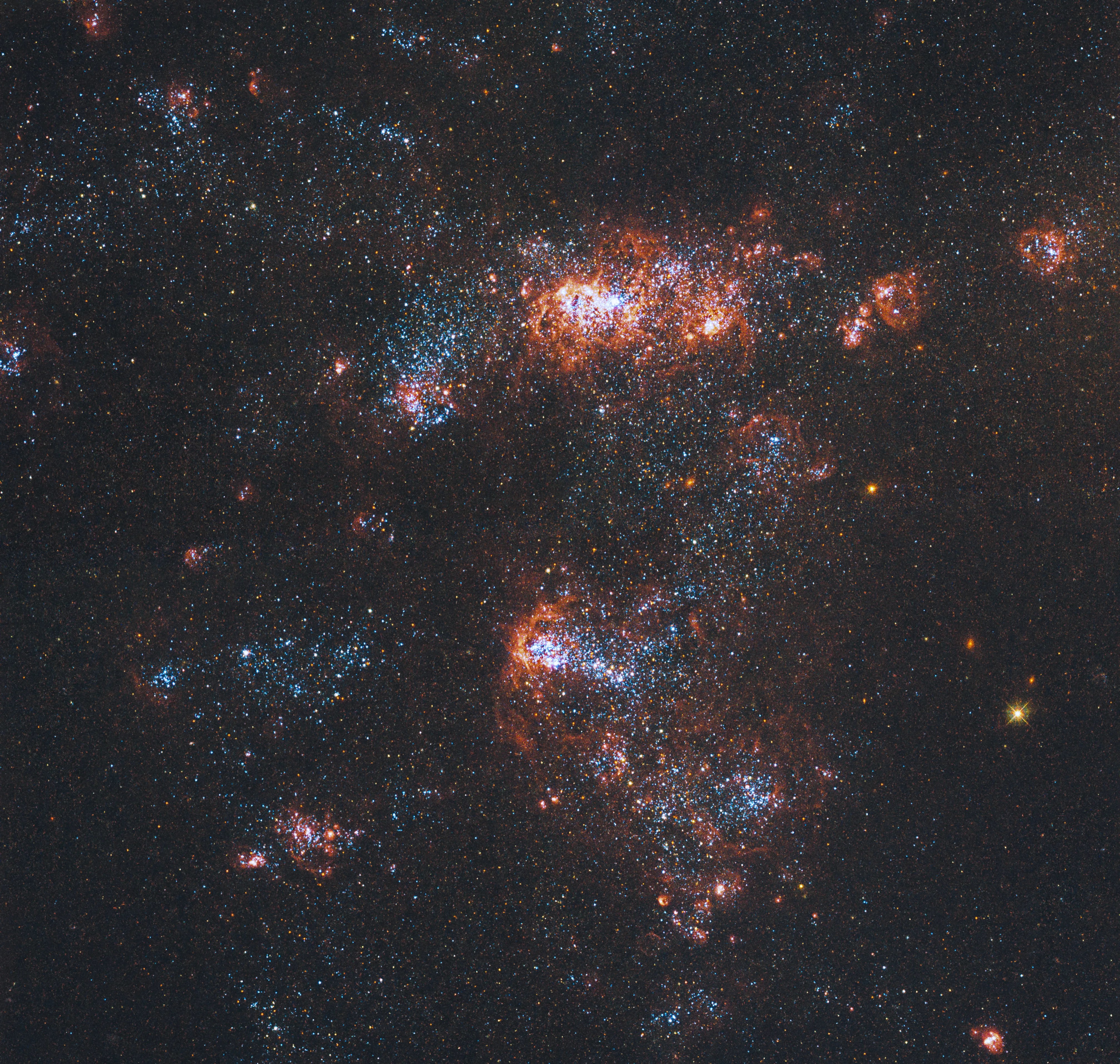 A patriotic groups of red, white, and blue stars, gas, and dust fills the scene on a black background. Groups of stars and gas are denser at image center. One lone yellow star shines toward the lower right.