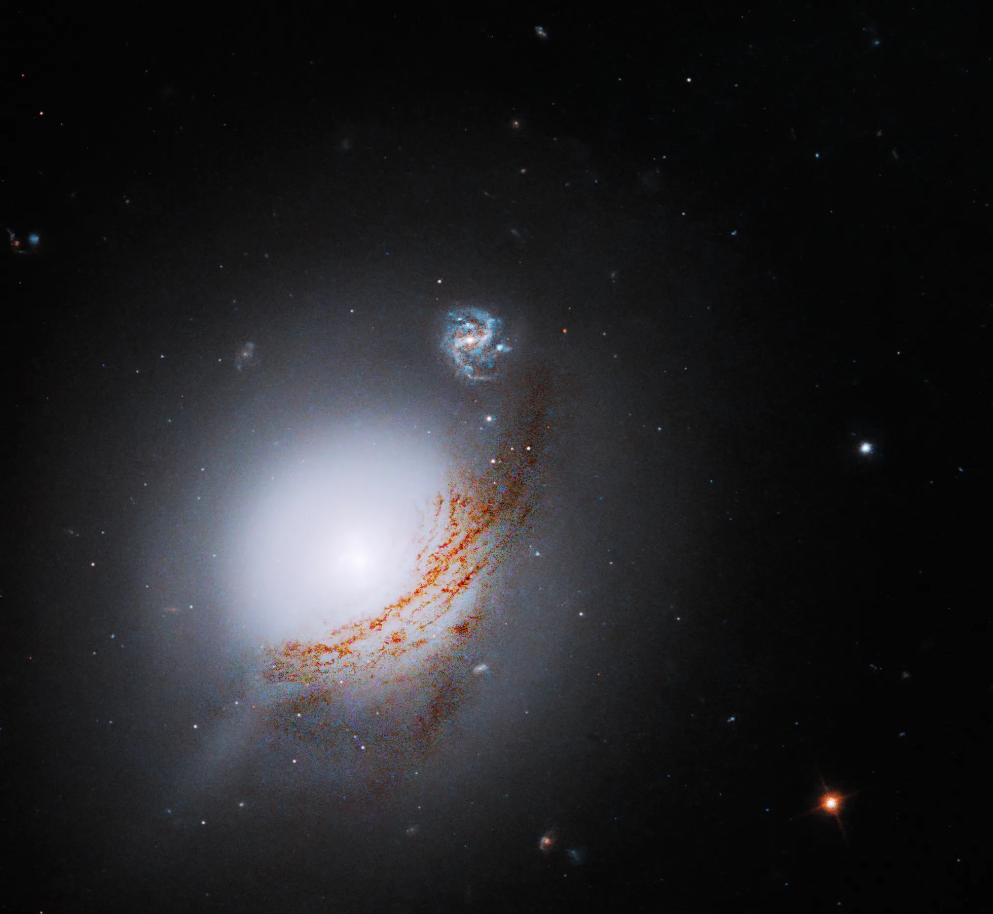 Lower left: Bright-white sphere of stars that is more diffuse toward its edges. Band of brown streaks arcs from the sphere's lower left to upper right where a face-on barred spiral galaxy shines in the distance. Black background dotted with stars.