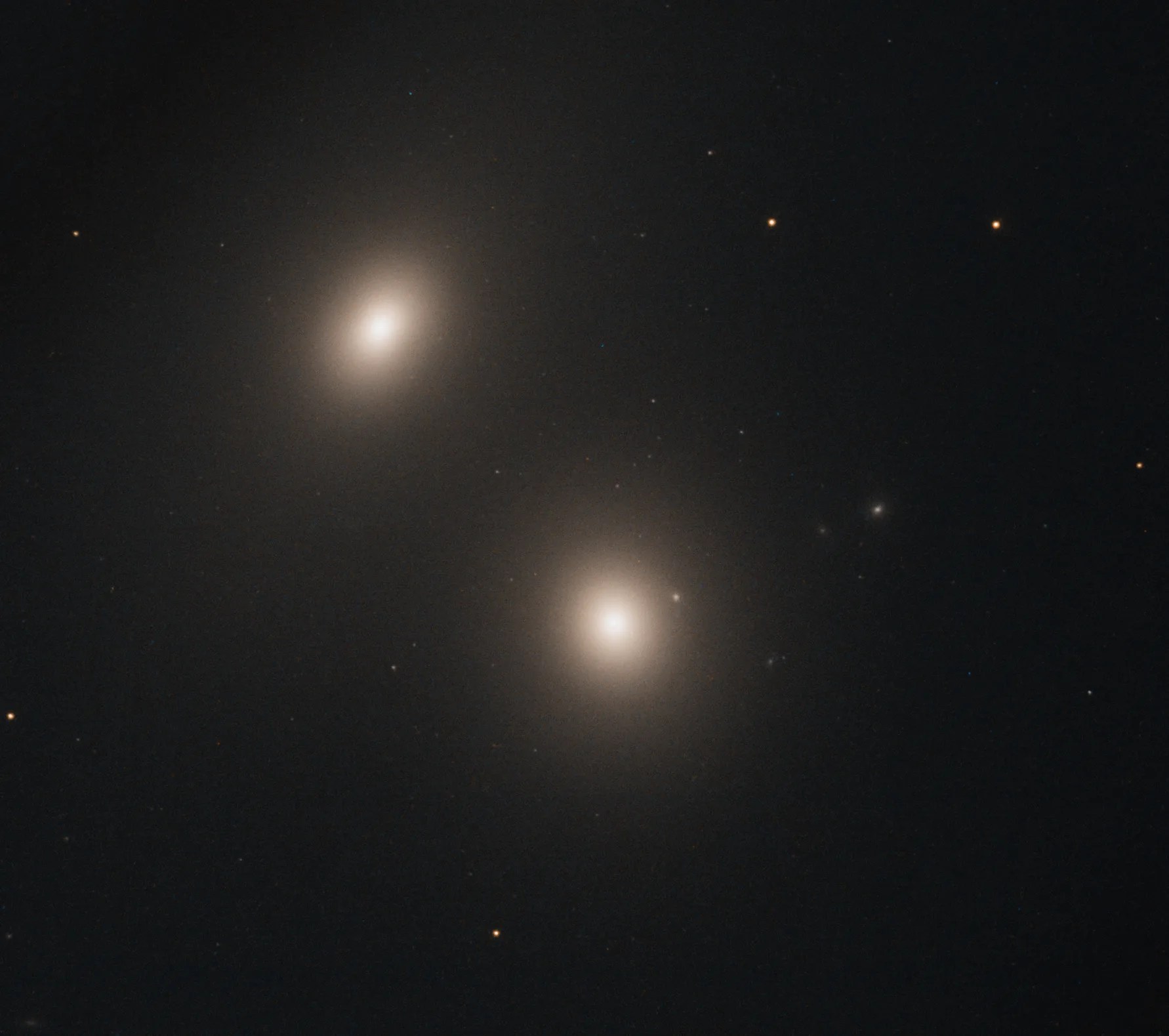 Two bright, oval blobs of stars. One right below image center, the other to the upper left. These blobs are galaxies with bright white centers that dims toward their edges. Black background dotted with stars.