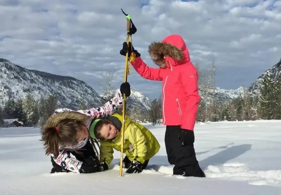 Three young girls measuring snow levels in a field of snow.