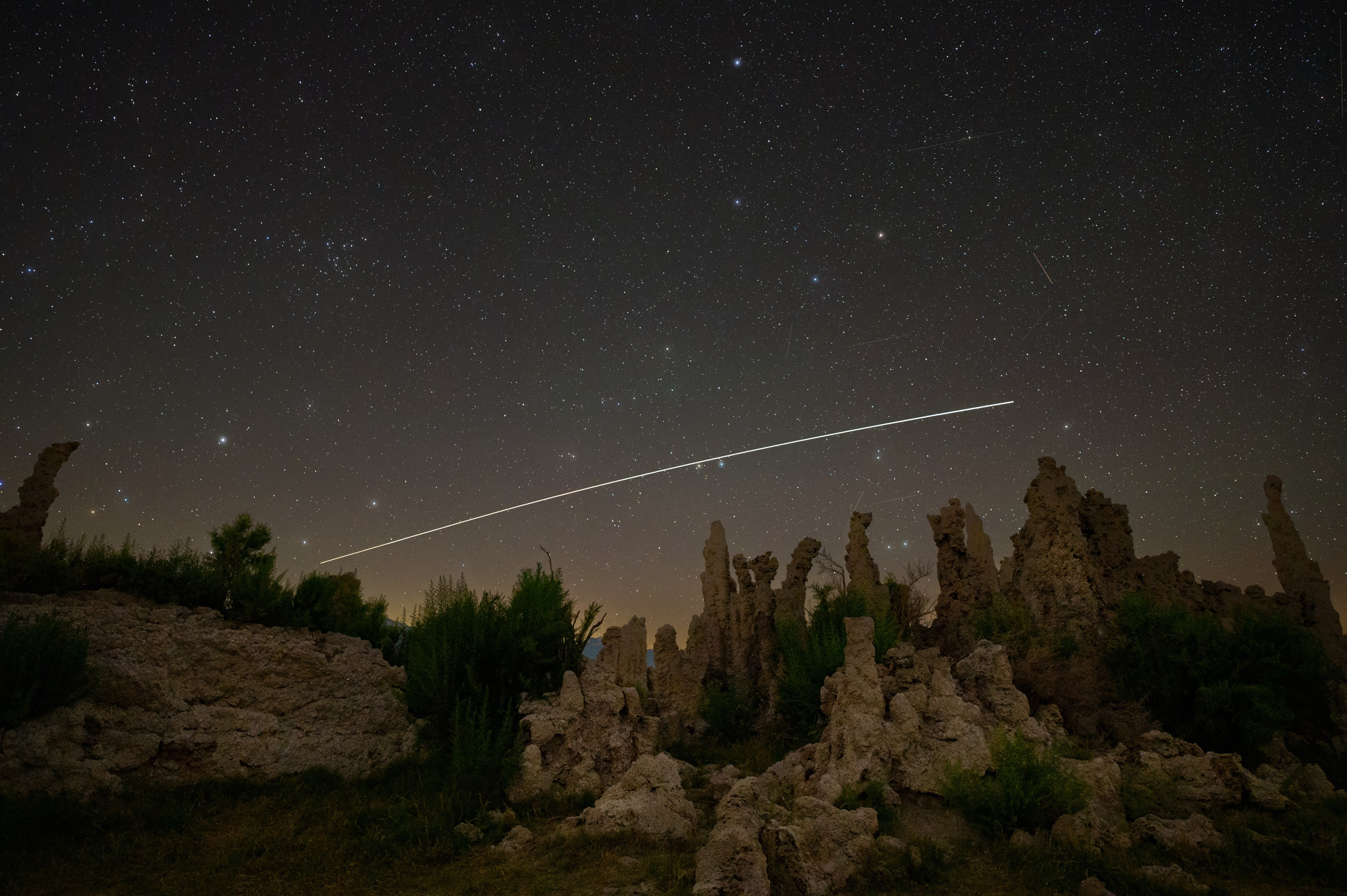 The International Space Station leaves a streak of light over a desert twilight landscape.