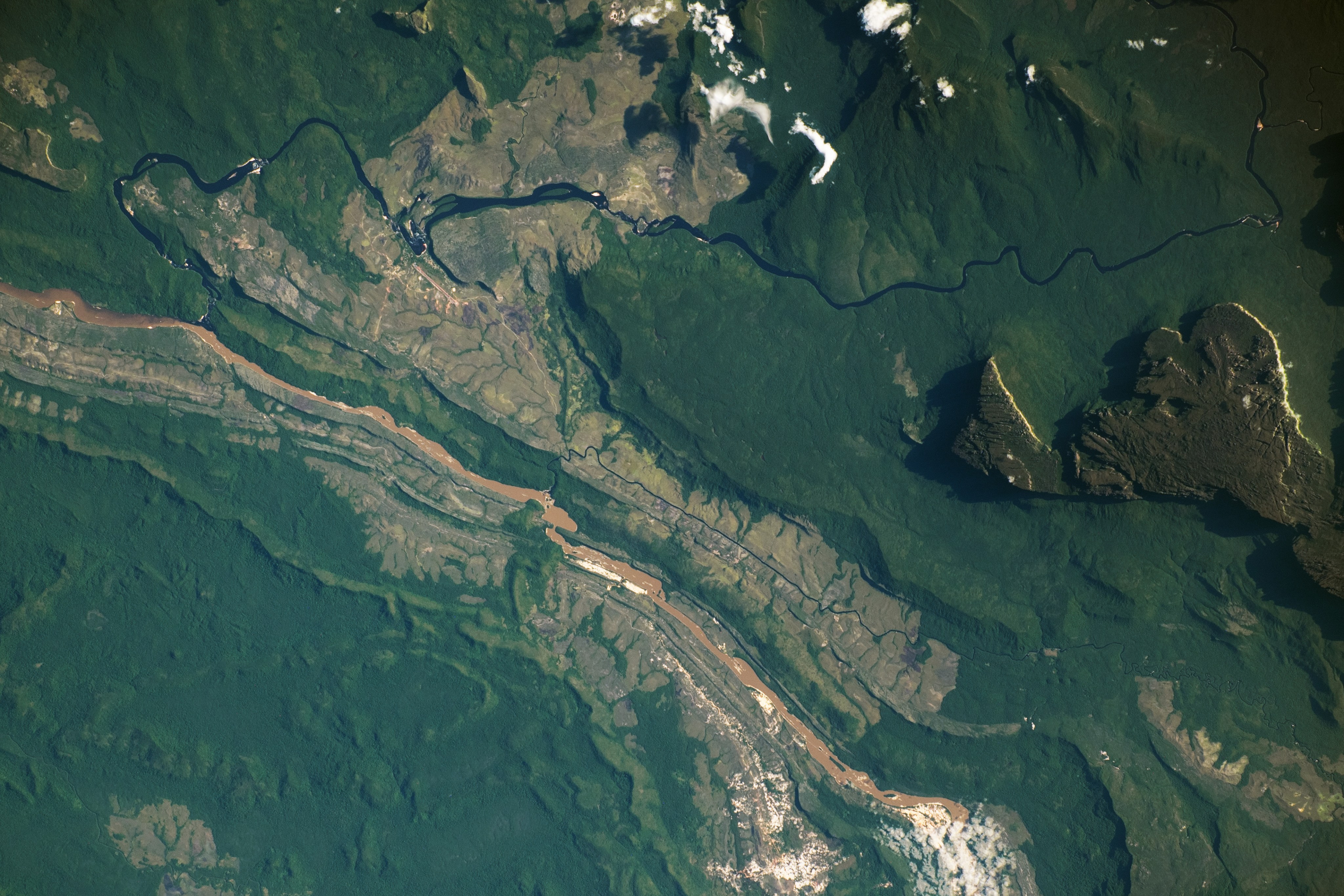 The Auyán-tepuí, also called Auyán Massif, towers thousands of feet above the surrounding area, casting shadows along its northern and western edges. The Caroní and Carrao rivers flow west of the massif, converging near Canaima and ultimately joining the Orinoco River.