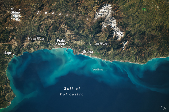 The Gulf of Policastro has medium blue waters with brighter water near the coast due to sediment. The land, occupying the upper half of the image, is mountainous, including Monte Sirino, snowcapped, in the top left. Sapri is noted on the coastline, farther right Praia a Mare, further right still Scalea. To the right of Scalea is the Lao River, and the Noce River is to the left of Praia a Mare.