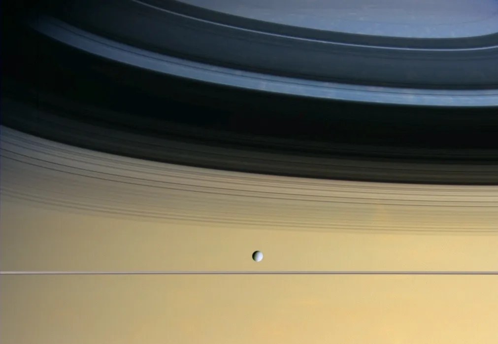 relatively tiny white moon floating before a colorful cloudscape on saturn