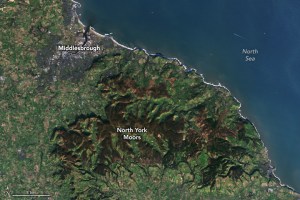 Land and sea meet diagonally from the center upper left to the bottom right. Along the coast, in the upper left, a human population center, Middlesbrough, is the one break amid rural farmland and the dark topped Moors. The Moors are situated below and to the right of Middlesbrough, following the coastline.