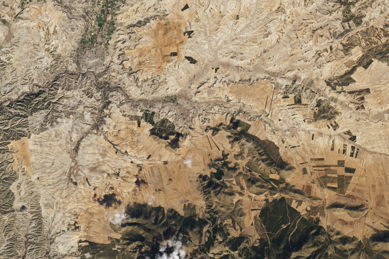 Satellite photo of largely dry light brown sandy Spain. A river runs from the middle left to the middle right side of the image and the land through this area is darker. A small dark patch of land is seen center left and bottom right there is another dark patch.