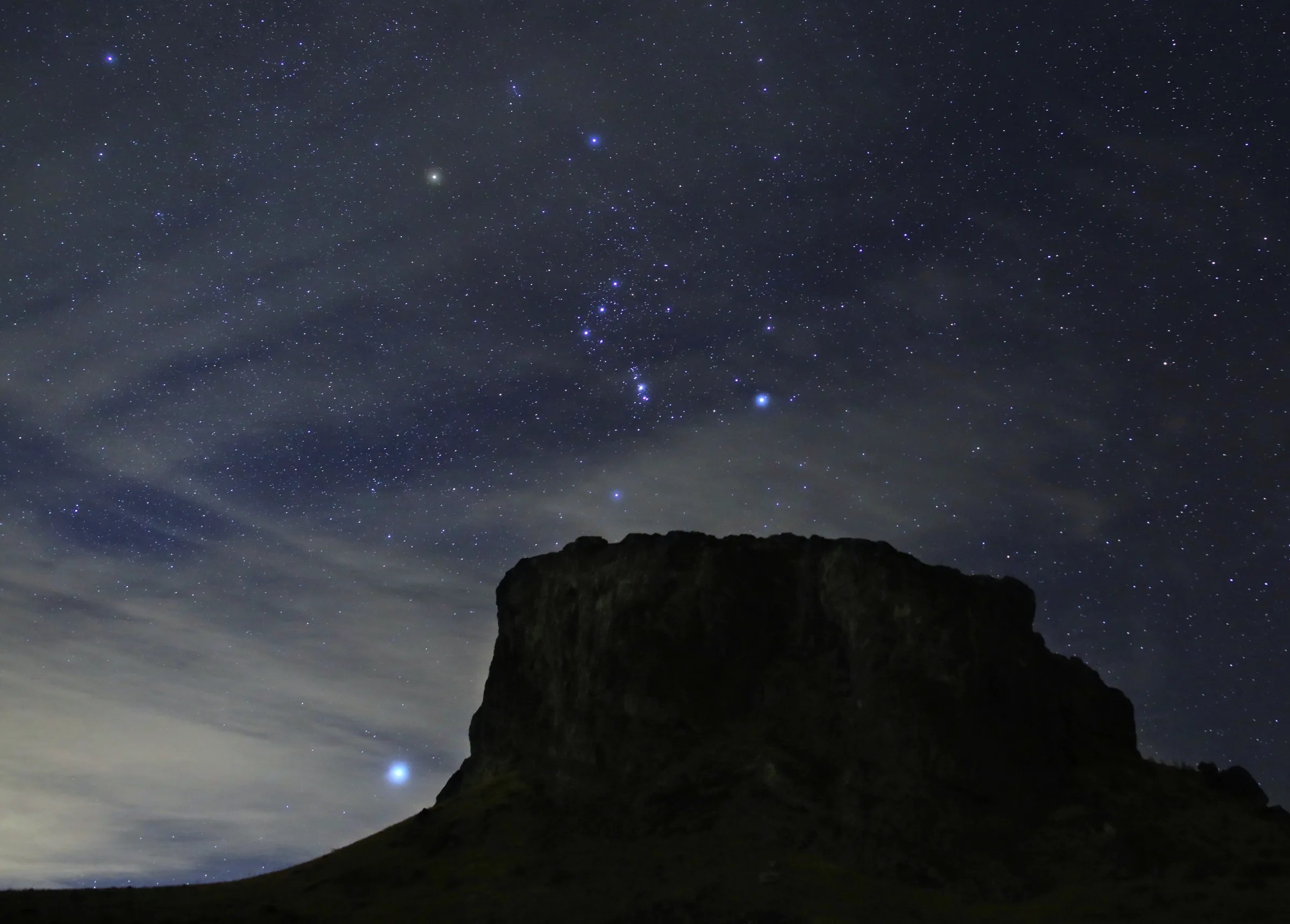 夜晚，猎户座中明亮的恒星出现在岩石台地上方。明亮的天狼星位于台地的左侧。