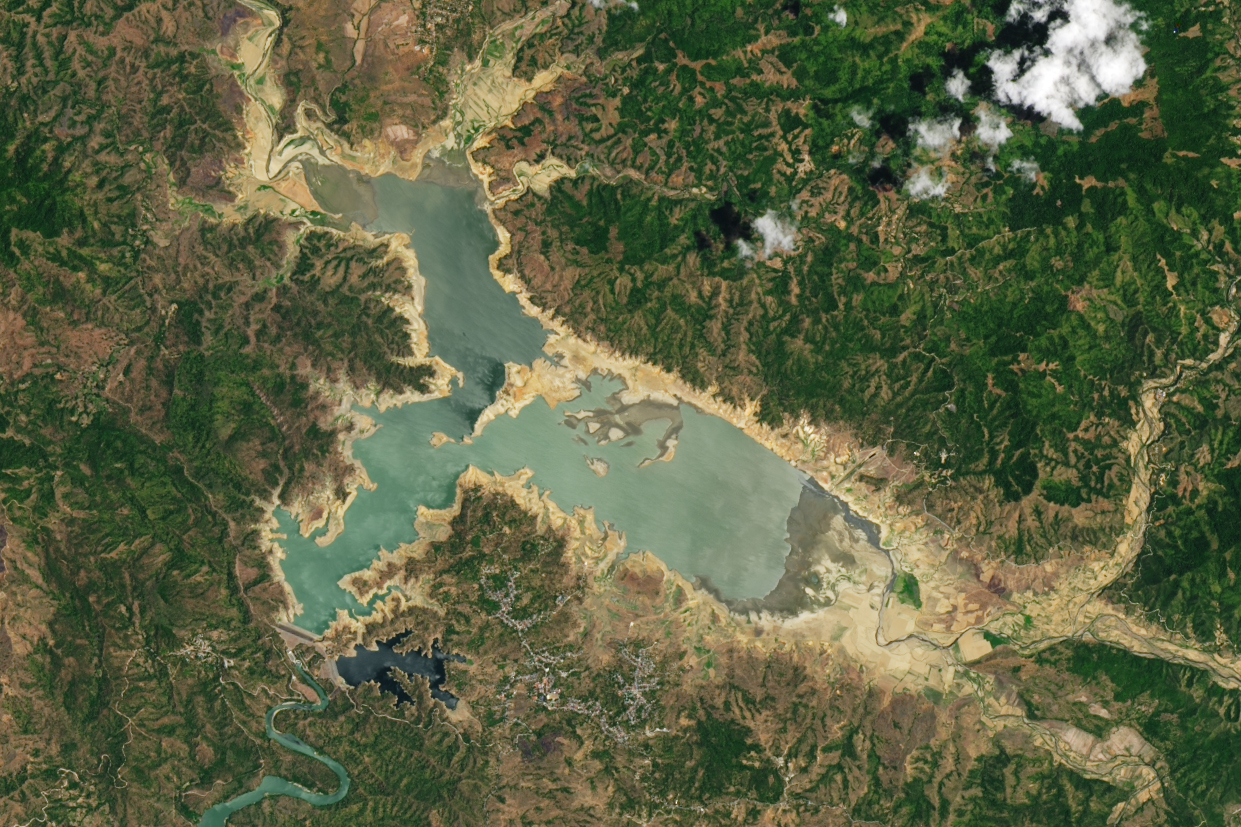 Pantabangan lake, surrounded by craggy land, brown peaks and green valleys give way to a significant amount of light tan sandy color soul that is typically under the waters of the lake. most notable to the right side of the image where the lake has it's most gradual depth change. However, what was once an island in the heart of the lake is now connected to the shore due to how much water levels have dropped.