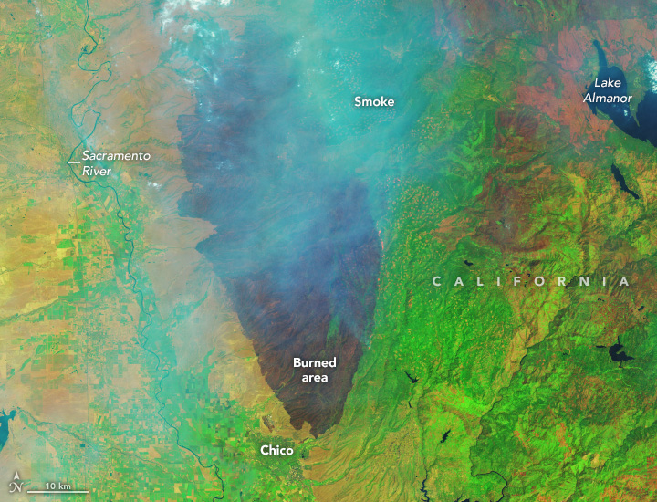 The satellite image centers a dark brown patch amid vibrant green landscape and runs largely parallel to the Sacramento River. The upper portion of the image is slightly obfuscated by smoke.